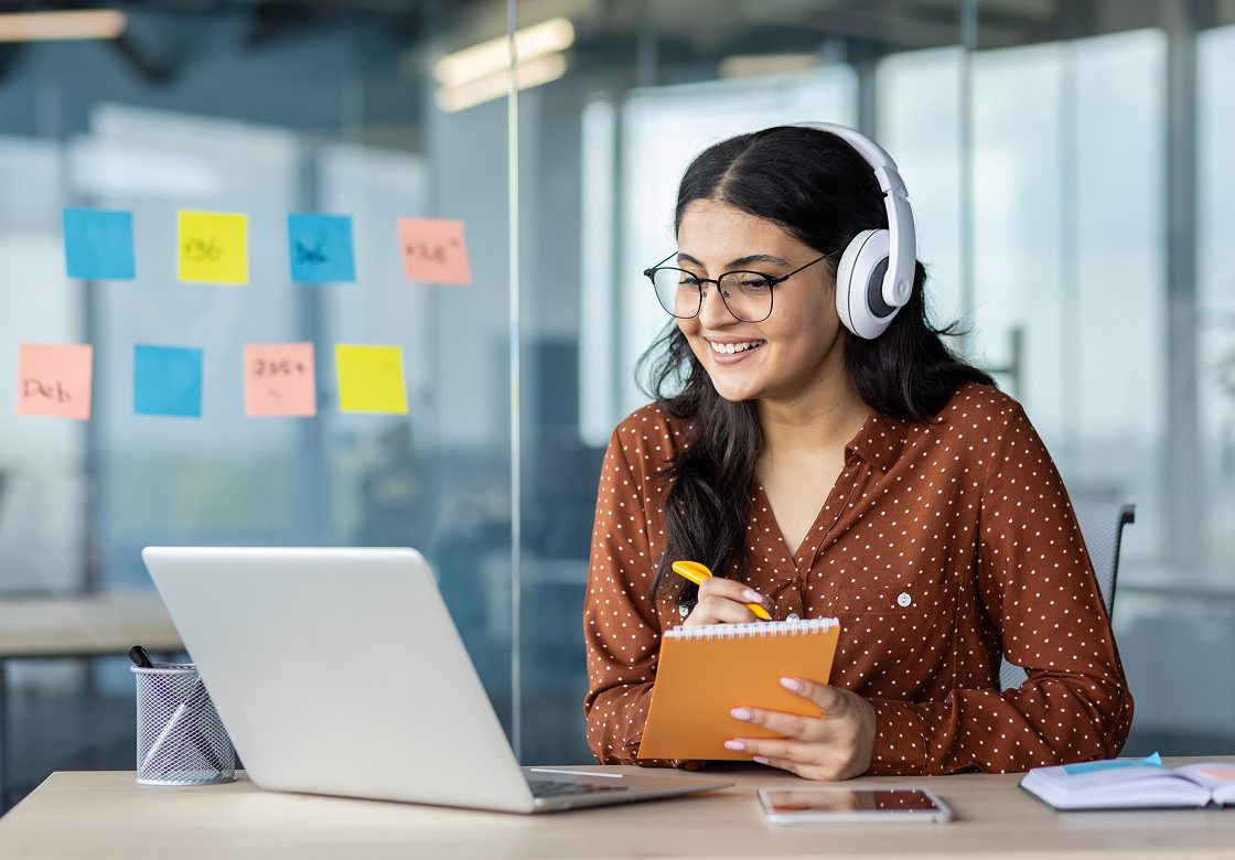 Woman with headphones taking notes online
